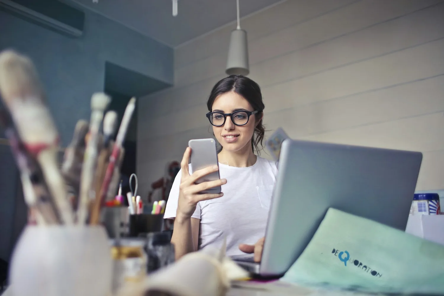 A small business owner checking her phone at her desk, laptop open